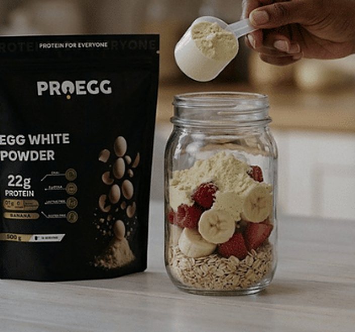 A scoop of ProEgg going into a jar of oats, banana and strawberries
